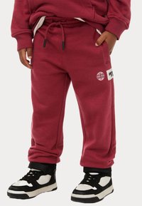 Bordeaux kleurige sweatpants met een verstelbare tailleband, zijzakken en een wit logo patch. Gepaard met zwart-witte hoge sneakers.
