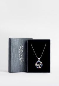 Silverhalsband med en cirkulär berlock, med ett stort "W" och färgade stenar som accentuerar kanten, visad i en svart låda.
