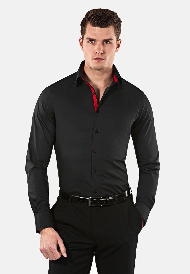 Chemise noire à manches longues avec des accents rouges sur le col et la patte de boutonnage, présentant une coupe ajustée et une texture lisse, associée à un pantalon noir.