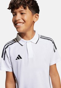 Polo bianco con accenti neri, dotato di colletto e tre strisce nere sulle spalle, realizzato in un materiale testurizzato e con logo di marca.