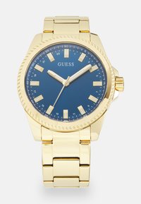 Reloj de pulsera de metal dorado con un dial azul, que cuenta con marcadores de hora blancos, agujas plateadas y un bisel texturizado, montado en una pulsera dorada.