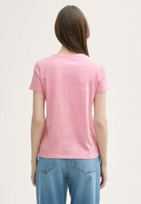 Camiseta de algodón rosa con escote redondo y mangas cortas, ajustada al cuerpo. Combinada con jeans de un azul claro, mostrando un aspecto casual.