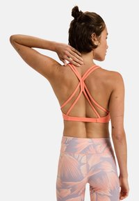Orange Sport-BH mit gekreuztem Rücken, kombiniert mit helllila Leggings mit einem Palmenblattmuster. Glatte Textur, figurbetonter Schnitt.