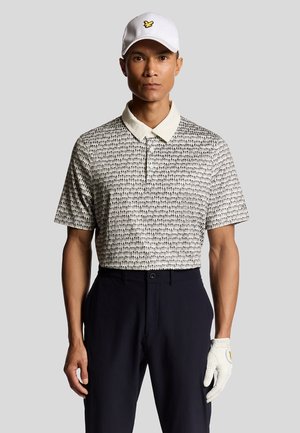 Short-sleeve polo shirt with a patterned design in black and white, cream collar, paired with dark pants and a white cap featuring a logo.
