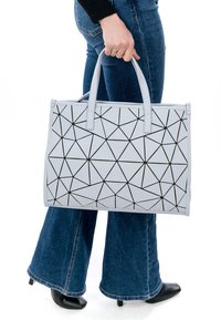 Grå geometriskt mönstrad tote-väska i läder med svarta linjer. Har två handtag och en strukturerad form. Positionerad vid höftnivå.