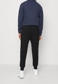 Granatowa bluza dresowa i czarne spodnie dresowe z elastycznymi mankietami i boczną kieszenią. Całość uzupełniają białe buty sportowe. Prosty, codzienny design.