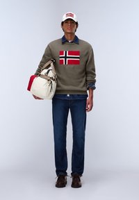 Grüner Pullover mit rotem, weißem und schwarzem Design der norwegischen Flagge, blaue Jeans, braune Schuhe und eine beigefarbene Tasche mit dunklen Akzenten.