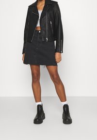 Černá kožená motorkářská bunda se stříbrnými zipy, šedý cropped top, černá džínová sukně s třepeným lemem a černé kotníkové boty s tlustou podrážkou.