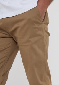 Beige chino kalhoty s hladkou texturou, slim fit, bočními kapsami a jemnými švy. Nosené s bílým tričkem.