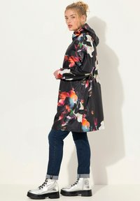 Bloemmotief waterdichte jas in het zwart, met levendige kleuren, een capuchon, lange mouwen en een trekkoord in de taille, gecombineerd met zilveren combat boots.