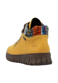 Botte cheville jaune avec un revers en tricot texturé multicolore, fermeture éclair sur le côté et semelle épaisse à rainures marron, vue en angle arrière.