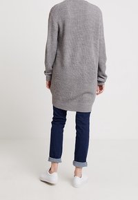 Długi szary sweter z dzianiny o prążkowanej fakturze, z wysokim kołnierzem i opuszczanymi ramionami. Połączony z podwiniętymi ciemnymi jeansami i białymi trampkami.