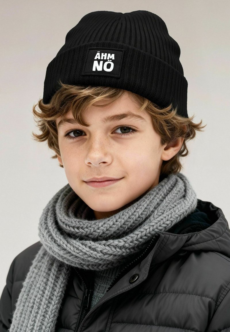 Black ribbed beanie with a white logo patch and a gray knitted scarf. The boy wears a black puffer jacket and has light curly hair.