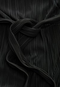 Tissu plissé noir à la texture lisse, présentant des sections entrelacées qui créent une profondeur et une dimension visuelle dans le design.