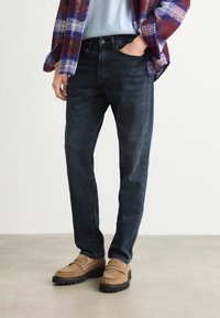 Σκοτεινές μπλε τζιν φτιαγμένες από τζιν, με κλασική γραμμή και σχέδιο πέντε τσέπες. Συνδυασμένα με καφέ λόφους και υπερδιάταξη ελεφαντόδοντου.