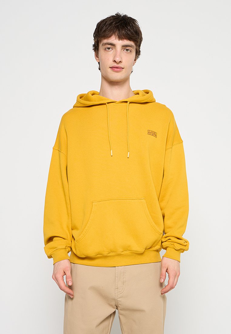 Geel capuchontrui met een voorzak, koordjes en een textuurstof. Bevat een klein logo op de linkerborst.