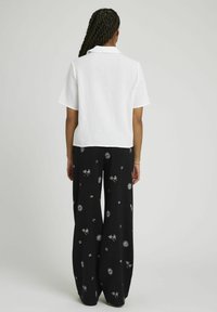 Chemise blanche à texture et à manches courtes associée à un pantalon large noir orné d'un motif floral et de soleils blancs.