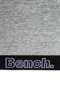 Sweatshirt gris avec un tissu texturé et une bande inférieure noire affichant "Bench." en lettres blanches brodées.