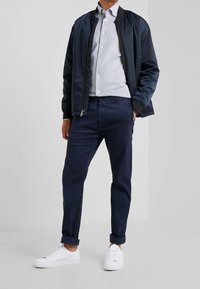 Granatowa kurtka bomberka z czarnymi mankietami, jasnoszara koszula z guzikami, granatowe spodnie i białe trampki. Gładki materiał, dopasowany krój, casualowy styl.