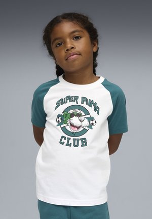 Dziecko z warkoczami, ubrane w białą i turkusową koszulkę "Super Puma Club" z wizerunkiem kreskówkowego pumy trzymającego w pysku piłki do piłki nożnej.