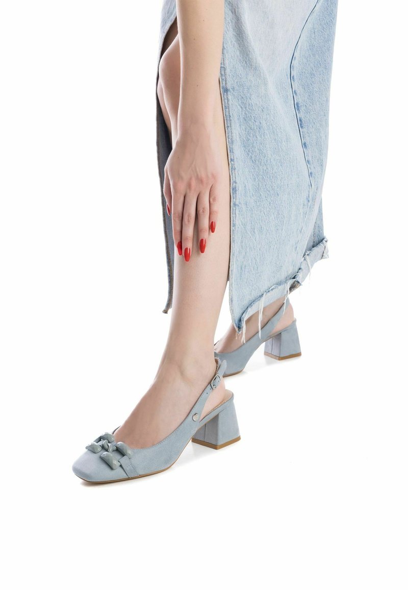 Zapatos slingback de ante azul claro con tacón cuadrado, decorados con dos lazos en la parte delantera. El tacón tiene una base beige contrastante.