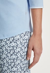 Lichtblauwe katoenen t-shirt met 3/4 mouwen en witte rand, gecombineerd met gestreepte pyjamabroekjes met marineblauwe bladeren op een lichte achtergrond.