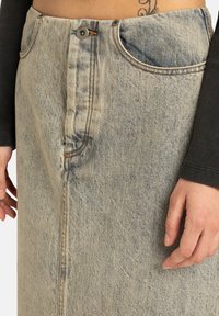 Gonna di jeans azzurro chiaro con vita alta, chiusura frontale con bottoni, due tasche laterali e cuciture visibili lungo le giunture.