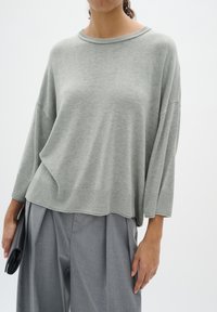 Light gray oversized sweater with a ribbed hem and cuffs, featuring a simple crew neckline and soft texture, paired with gray pleated trousers.