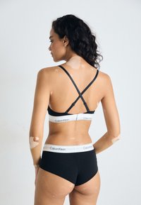 Soutien-gorge en coton noir et culotte assortie, dotés d'une taille en élastique blanche "Calvin Klein" et de bretelles croisées dans le dos. Texture lisse, design minimal.