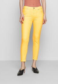 Gula smala jeans med en slät yta, med en standard femficksdesign och en knäppning i midjan, tillsammans med svarta skor.