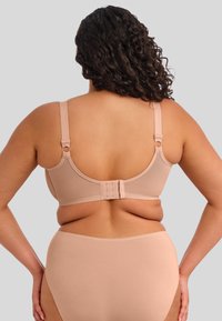 Soutien-gorge nude et culotte taille haute assortie fabriqués en tissu lisse. Le soutien-gorge dispose de bretelles ajustables et d'une fermeture à plusieurs crochets au dos.