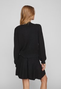 Schwarzer gestrickter Pullover mit langen Ärmeln und dezenten Puffärmeln, kombiniert mit einem ausgestellten schwarzen Rock. Weiche Textur, lässiges Design.