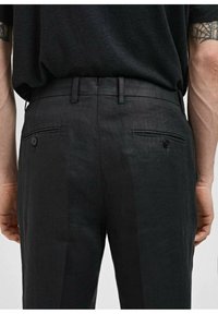 Zwarte linnen broek met een gestructureerd oppervlak, voorzien van twee achterzakken met knopen en een slim-fit ontwerp. Ceintuurlussen rond de taille.