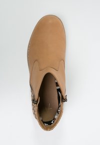 Tan nahkasaapas nilkkamittaisella varrella, pyöreällä varvalla, sivuvetoketjulla ja teksturoidulla, kudotulla takana. Sisäpuolella on kuviollinen vuori.