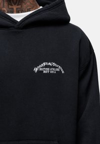 Felpa nera in cotone con un logo ricamato bianco curvo "GOOD FOR NOTHING BRITISH ATELIER EST 2011" sul petto.