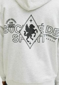 Jasnoszara bluza z kapturem z czarnym graficznym motywem lwa w kształcie diamentu, uzupełniona tekstem i akcentami w formie gwiazdek, wykonana z miękkiego materiału bawełnianego.