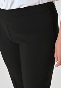 Zwarte op maat gemaakte broek van een gladde stof, met een slim fit, tailleband en een subtiele zijrits voor gemakkelijk aantrekken.