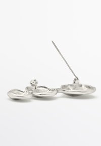 Silver metal brooch in an abstract floral shape, featuring textured petal-like elements and a pointed pin for attachment.