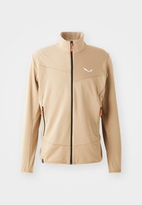 Beige softshell jakke med høy krage, svart glidelås og to sidelommer med oransje detaljer. Har et subtilt teksturert mønster.