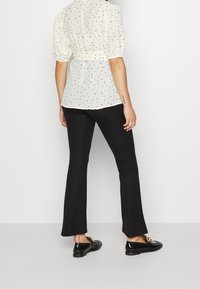 Camicia color avorio chiaro con pois neri, maniche a sbuffo e vita aderente, abbinata a pantaloni neri svasati e mocassini neri lucidi.