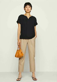 Top negro de manga corta con escote en V, combinado con pantalones beige ajustados y un bolso naranja de forma redondeada. Sandalias negras de dedo al aire completan el look.