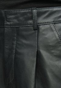 Μαύρο δερμάτινο παντελόνι με λεία υφή, με επίπεδη μπροστινή σχεδίαση, ραμμένη μέση και πλαϊνές τσέπες.