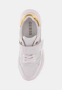 Białe sneakersy Guess z grubą podeszwą, złotym akcentem na pięcie, wytłoczoną paskiem, białymi sznurówkami i logo nadrukowanym wewnątrz.