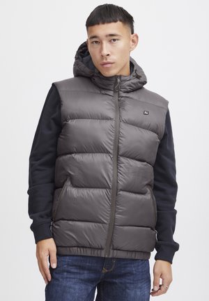 Grå quiltet puffervest med hette, som har glidelås foran, sidelommer og kontrasterende marineblå ermer. Glatt, glanset stofftekstur.