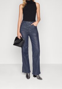 Ciemne szerokie spodnie dżinsowe zestawione z fakturowanym czarnym topem bez rękawów, uzupełnione małą czarną torebką i srebrnymi botkami na obcasie.