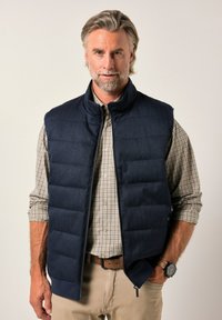 Marinblå puffväst med hög krage, med kviltade sektioner, dragkedjestängning och sidofickor. Bärs över en rutig knäppskjorta.