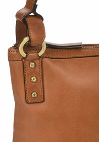 Bolso de mano de cuero color tan con una textura suave, que presenta un anillo cilíndrico y tres tachuelas circulares en tono dorado en el punto de unión de la correa.