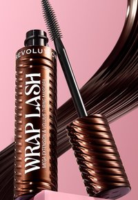 Brauner zylindrischer Mascara-Tube mit spiralförmigen Rillen, schwarze Bürste mit spitzen Borsten, vor einem pinken Hintergrund. Text: "WRAP LASH."