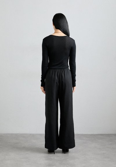 Black long-sleeve top paired with loose-fitting black pants. The fabric appears soft and textured, with an elastic waistband and cuffed sleeves.