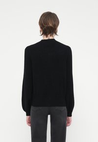 Black knitted sweater with a round neckline, long sleeves, and a fitted bottom hem. Soft texture with no visible patterns or accents.